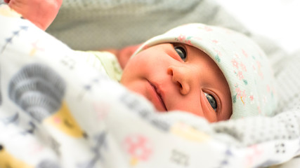 A newborn beautiful baby looking smart at the camera in light green colors. Closeup.