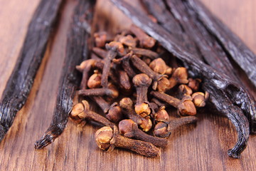 Cloves and fragrant vanilla on wooden board