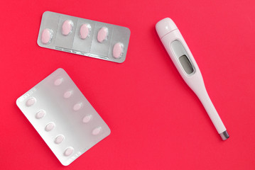 Thermometer and silver blisters with pills on a red background. Pharmacy and medical concept. Flat lay, top view