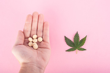 concept: natural medicine and chemical, the right choice for patients with cancer. pills in the palm and cannabis leaf on a pink background.