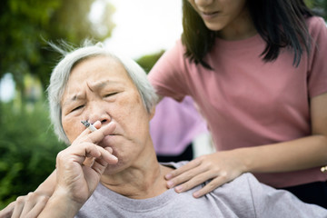 Asian senior grandmother hold a cigarette smoking,old people or smoker smoking near granddaughter,child girl request elderly woman to stop smoking, bad smell,smelling pollution, health care,lifestyle