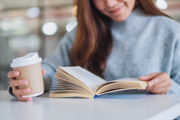 Closeup image of a woman reading a book while drinking coffee on wooden table