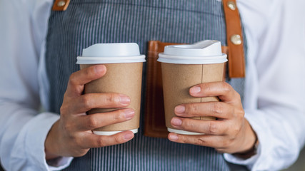 A waitress holding and serving two paper cups of hot coffee in cafe