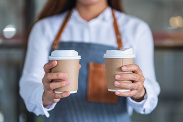 A waitress holding and serving two paper cups of hot coffee in cafe