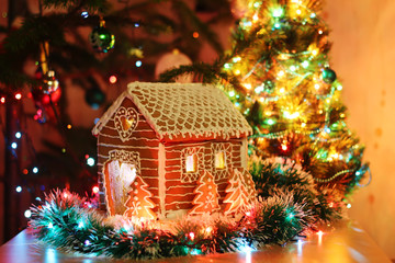 Gingerbread house with icing. Festive evening tree with lights and garlands.