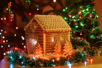 Gingerbread house with icing. Festive evening tree with lights and garlands.