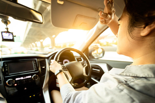 Asian female driver covering face by hand of bright sun,disturbed dazzled by sun light,difficulty in driving,young woman driving car feeling hot uncomfortable,risk of eye damage from ultraviole,UV ray