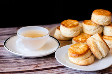 White cup of hot tea and Fresh Homemade delicious butter scones on wooden table with black background. Traditional British Scones perfect combination for tea time.
