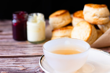 White cup of hot tea and Fresh Homemade delicious butter scones on wooden table with black background. Traditional British Scones perfect combination for tea time.