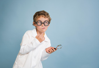 Funny boy scientist in lab coat holding magnifying glass with silly thinking expression