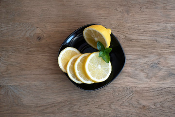Fresh mint herb and lemon in a black plate on wooden background.