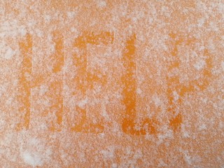 Word snow covered HELP written by hand on an orange metal surface covered with hoarfrost. View from above.
