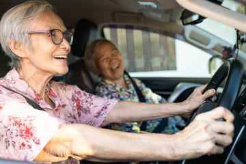 Happy smiling asian senior female driver in her car,enjoy traveling during retirement age with her friend,healthy old people having fun together,elderly woman driving car,road trip,travel concept