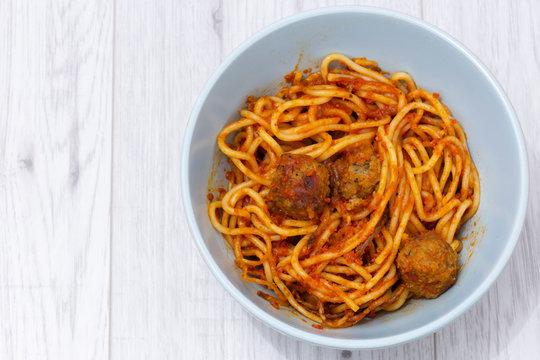 Spaghetti with meatballs in a tomato suce with herbs and spices in a green bowl.  On a grey wood surface