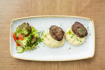 Delicious juicy meat cutlets, mashed potatoes sprinkled with greens and fresh healthy salad of tomatoes and lettuce leaves.