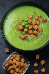 Black bowl of green peas cream-soup with croutons, vertical shot, close-up