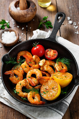 Prawns Shrimps roasted on frying  pan with lemon and garlic on wooden background.