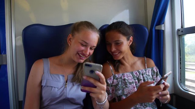 cute blonde in summer dress shows funny picture to girl teenager friend on phone riding intercity train closeup