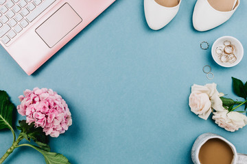 Beautiful feminine flatlay of pink laptop and woman's white shoes, jewerly and flowers on blue,...