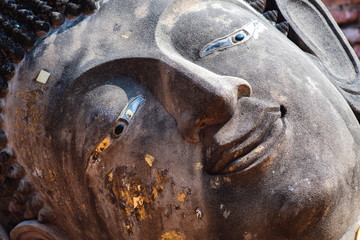 Close up face of ancient old face Buddha statue with gold leaf foil at thailand temple.