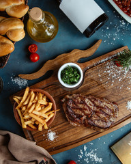 beef steak served with french fries and diced gren herbs on wooden board