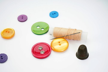 Sewing supplies. Thimble, thread, needle and different buttons on a light background.