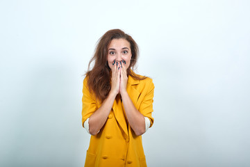 Attractive young woman in yellow jacket covering eyes mouth with hands, looking shocked isolated on gray background in studio. People sincere emotions, lifestyle concept.