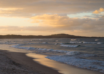 River mouth feeding into the ocean at dusk with surfers catching the last few waves of the day