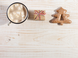 Hot Christmas drink with marshmallows in an iron mug and gingerbread cookies, on a white table. New Year, holiday background, copy space.