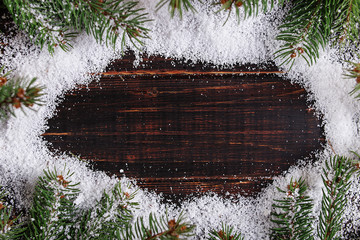 Christmas background frame, green Christmas trees on a wooden table, dashed by white snow, copy space, top view.
