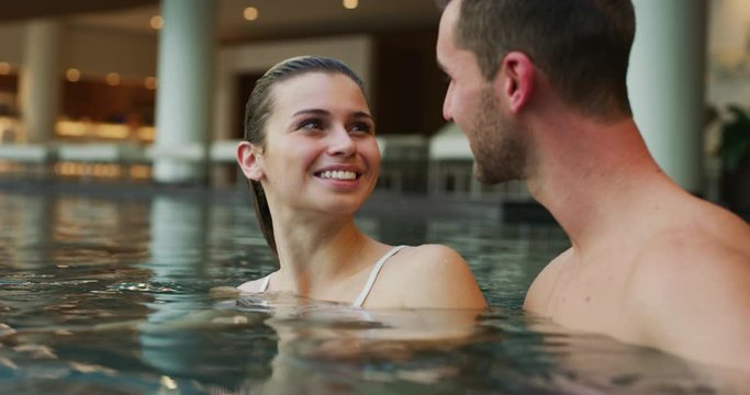 An young couple is embracing and having relax in an indoor illuminated with night lights swimming pool in a luxury wellness center.
