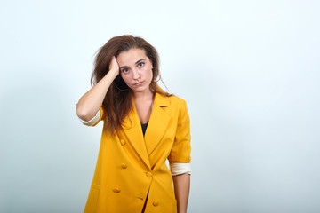 Mad young woman in yellow jacket keeping hand on head, looking angry isolated on gray background in...