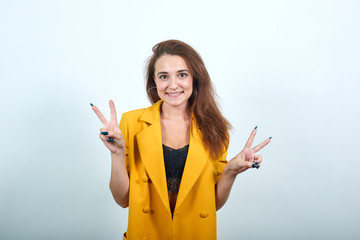 Cheerful young woman in yellow jacket isolated on gray background in studio, showing victory...