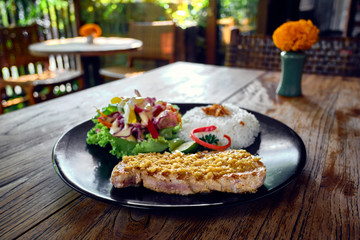 Grilled tuna steak with rice and vegetables in interior of a cafe.