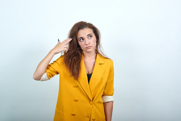 Unhappy young woman in yellow jacket looking dissatisfaction, keeping hand on head like gun...