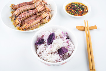 A plate of steamed crusty prawns and a bowl of purple potato rice on white background
