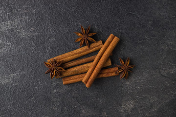 Cinnamon sticks and anise stars on a black stone background.