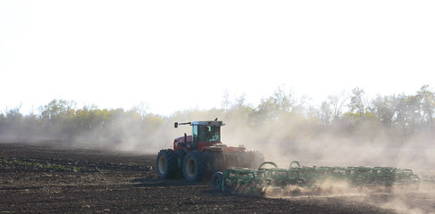 preparation of the field by the farmer by disking the soil on a tractor, the dust being raised is illuminated by the sun