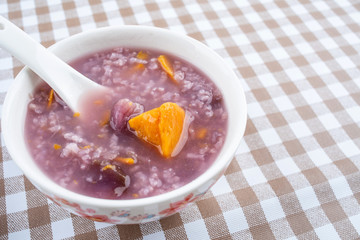 A bowl of nutritious and healthy boiled purple potato porridge on a plaid table top