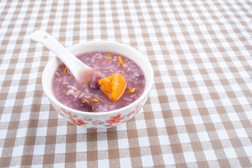 A bowl of nutritious and healthy boiled purple potato porridge on a plaid table top