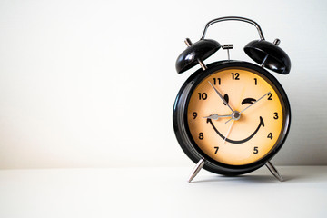 black alarm clock with a yellow dial and a smiley face on a white background