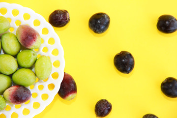 natural round green and brown olives in a decorative plate on a yellow background