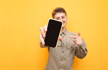 Smartphone with a dark screen in the hand of a cheerful young man stands on a yellow background....