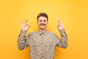 Happy young man in shirt and glasses smiling, looking at camera and showing thumbs up gesture OK on...