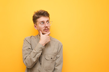 Portrait of surprised nerd student in glasses and shirt on yellow background, looking away at copy space with emotional face. Charismatic guy with mustache looks surprised at the yellow background.