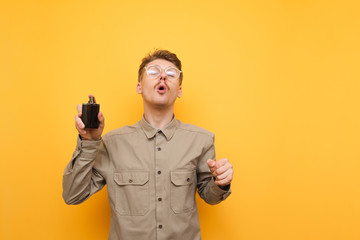 A funny nerd in a shirt and glasses uses perfume on a yellow background. Guy with the mustache...