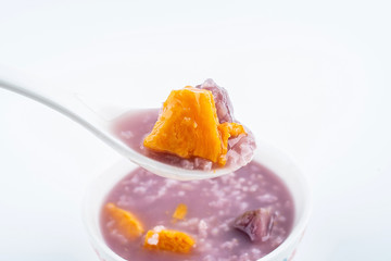 Hand holding a spoonful of nutritious and delicious sweet potato porridge on white background