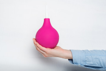Big pink enema in a female hand. White background. Medical item