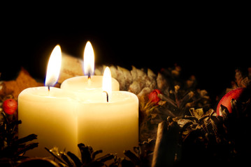 three burning candles with Christmas decoration from pine cones around