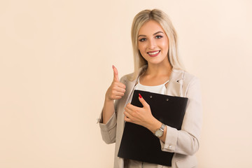 beautiful young woman in suit with folder on beige background with hand gesture